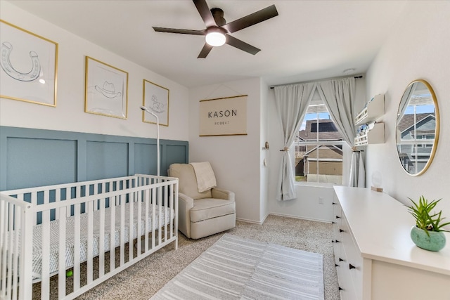 bedroom featuring a nursery area, light colored carpet, a decorative wall, and ceiling fan