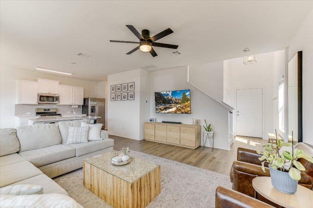 living area with stairway, visible vents, light wood finished floors, and ceiling fan