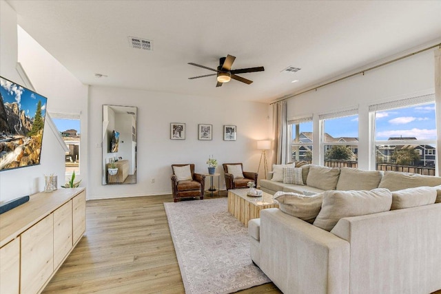 living room with a ceiling fan, visible vents, and light wood finished floors