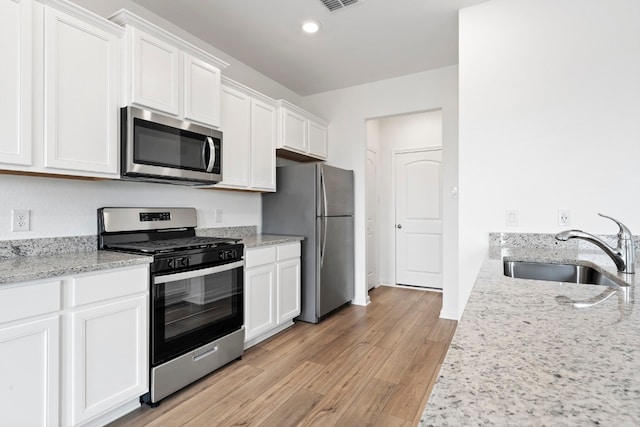 kitchen with a sink, white cabinets, appliances with stainless steel finishes, light wood-type flooring, and light stone countertops