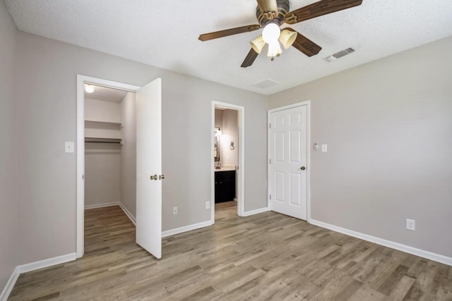 unfurnished bedroom with light wood-style flooring, a spacious closet, visible vents, and baseboards