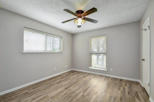 spare room with a wealth of natural light, a textured ceiling, baseboards, and wood finished floors