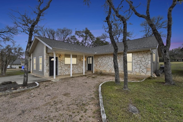 single story home with stone siding, a shingled roof, and a porch