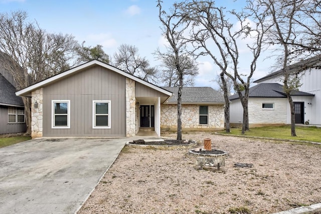 view of front of property featuring stone siding, a fire pit, and roof with shingles