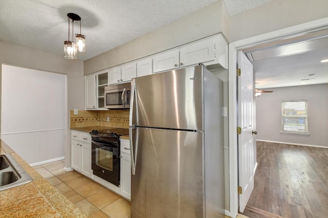 kitchen with stainless steel appliances, a textured ceiling, light countertops, white cabinetry, and backsplash