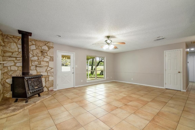 unfurnished living room featuring light tile patterned floors, visible vents, a ceiling fan, a wood stove, and a textured ceiling