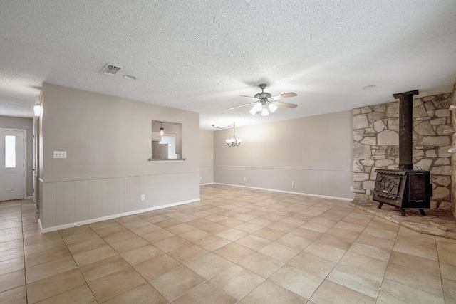 unfurnished living room with visible vents, a wood stove, ceiling fan with notable chandelier, a textured ceiling, and light tile patterned flooring