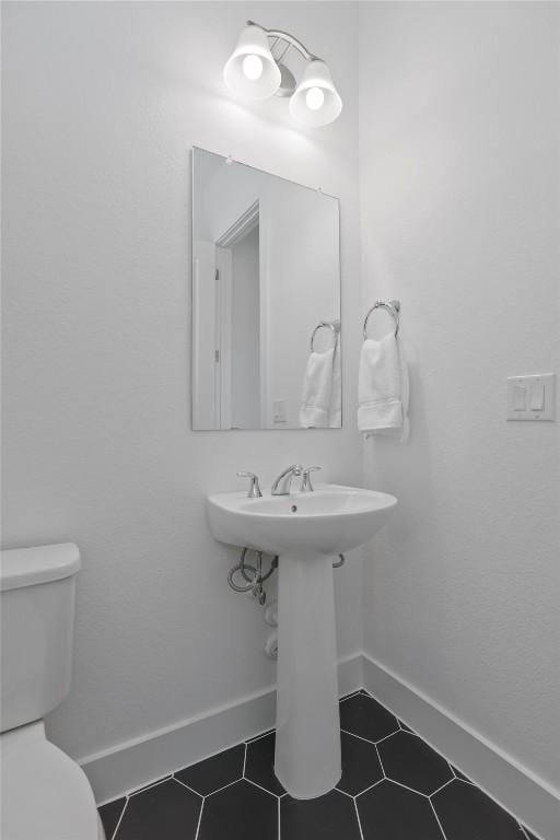 half bath with baseboards, toilet, and tile patterned floors