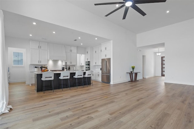 kitchen featuring appliances with stainless steel finishes, a breakfast bar area, light countertops, light wood-type flooring, and premium range hood