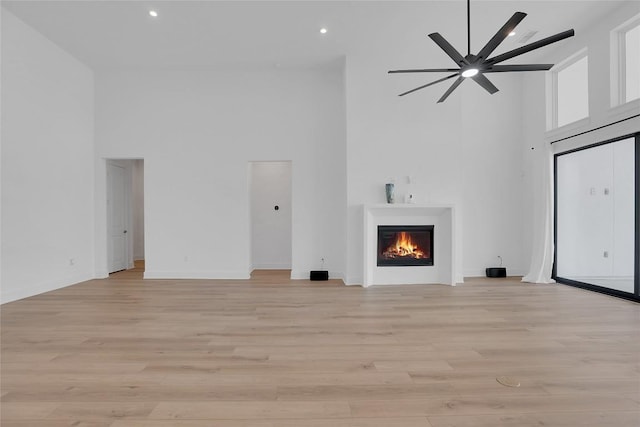 unfurnished living room with a towering ceiling, a warm lit fireplace, light wood-style flooring, and recessed lighting