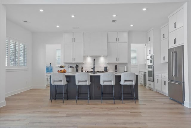 kitchen featuring an island with sink, high end refrigerator, white cabinets, and light countertops