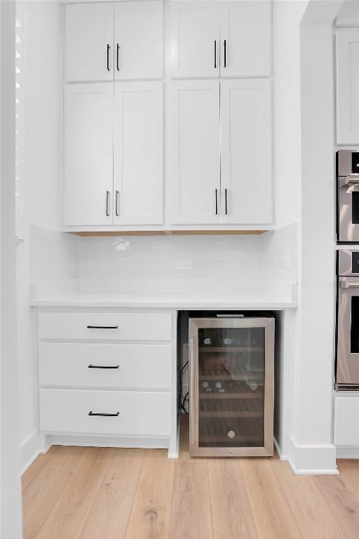 bar featuring beverage cooler, stainless steel double oven, and light wood-style floors