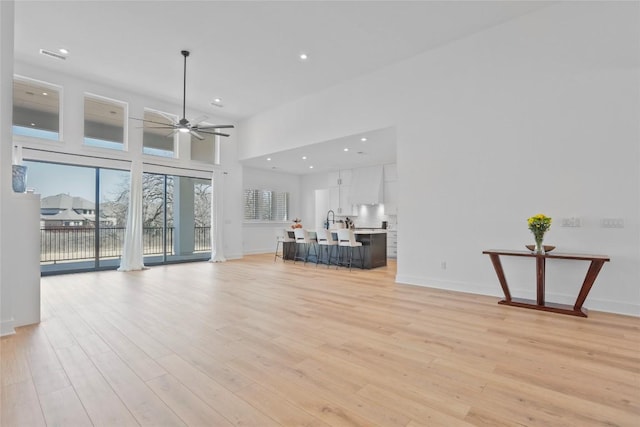 unfurnished living room featuring recessed lighting, a high ceiling, a ceiling fan, baseboards, and light wood-style floors