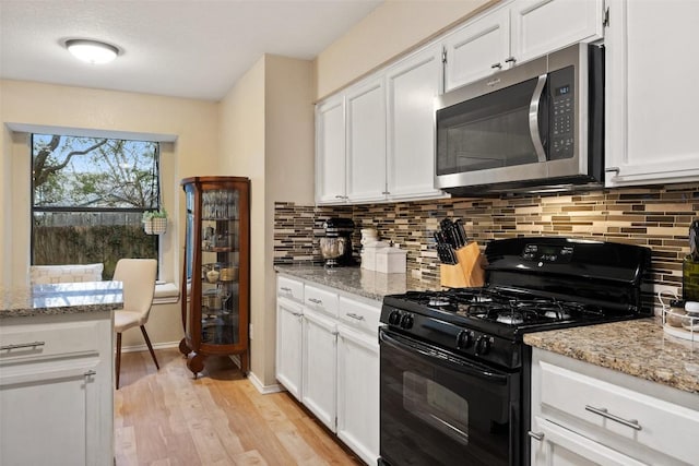 kitchen with light wood finished floors, stainless steel microwave, black range with gas stovetop, and decorative backsplash