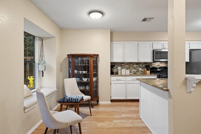 kitchen featuring visible vents, black stove, stainless steel microwave, light wood-type flooring, and white cabinetry