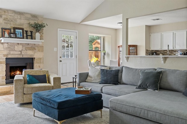 living area featuring lofted ceiling, light wood-type flooring, a fireplace, and visible vents