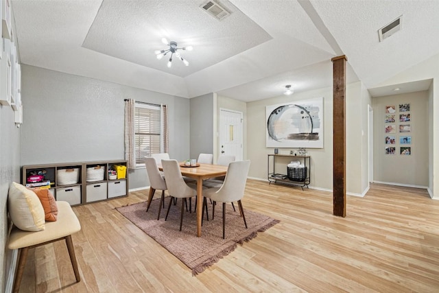 dining area with light wood-style floors, a tray ceiling, visible vents, and a textured ceiling