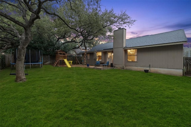 yard at dusk with a patio area, a fenced backyard, a trampoline, and a playground