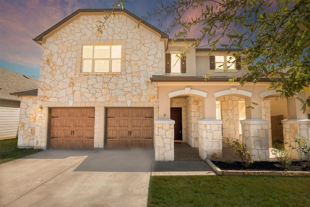 view of front of house featuring a garage, concrete driveway, stone siding, and stucco siding