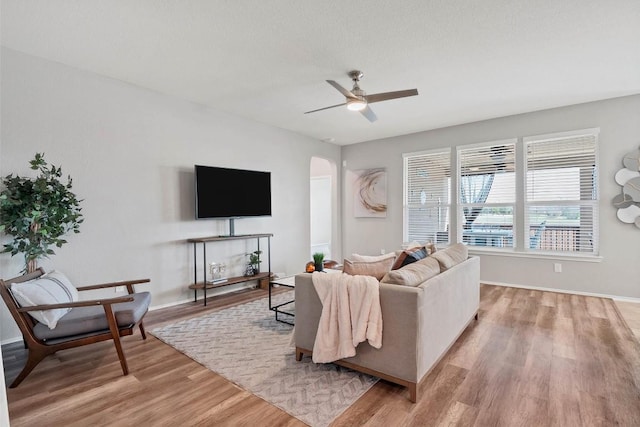 living room featuring light wood-style floors, ceiling fan, arched walkways, and baseboards