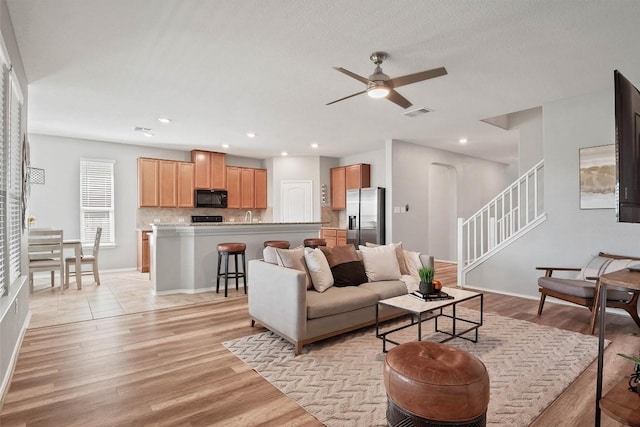 living room featuring a ceiling fan, light wood-type flooring, recessed lighting, and stairs