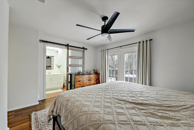 bedroom featuring a barn door, ceiling fan, connected bathroom, wood finished floors, and access to outside