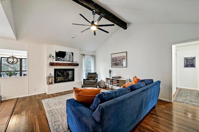 living area with lofted ceiling with beams, ceiling fan with notable chandelier, dark wood-type flooring, baseboards, and a brick fireplace