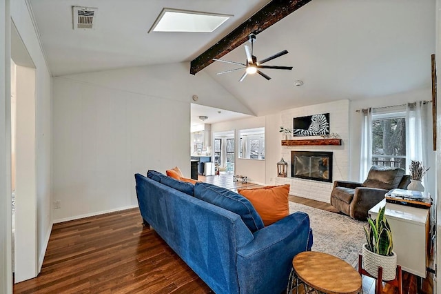 living area with visible vents, a ceiling fan, dark wood-style floors, lofted ceiling with skylight, and a brick fireplace