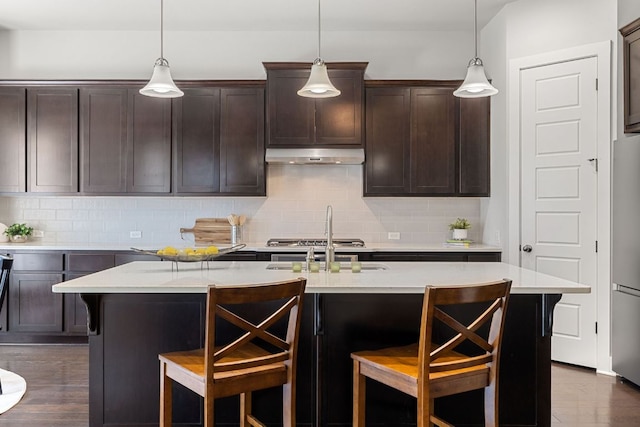 kitchen featuring dark wood-style floors, a breakfast bar, appliances with stainless steel finishes, dark brown cabinets, and under cabinet range hood