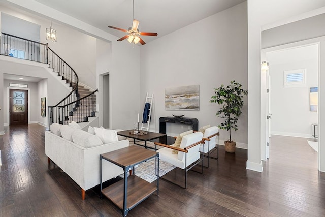 living room with baseboards, dark wood finished floors, stairway, a high ceiling, and ceiling fan with notable chandelier