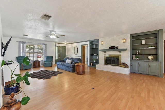 living area with visible vents, a fireplace, a textured ceiling, and light wood finished floors