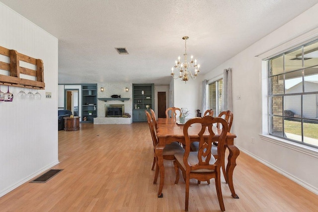 dining area with light wood-type flooring, a brick fireplace, visible vents, and a textured ceiling