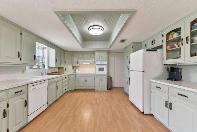 kitchen with a raised ceiling, visible vents, a sink, white appliances, and under cabinet range hood