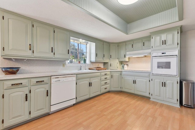 kitchen with a tray ceiling, light countertops, light wood-style floors, white appliances, and under cabinet range hood