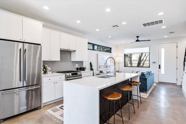 kitchen with stainless steel appliances, visible vents, a sink, concrete flooring, and a kitchen breakfast bar