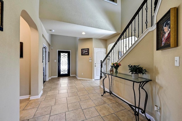 entryway with arched walkways, stairway, light tile patterned flooring, and baseboards