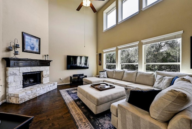 living room with baseboards, dark wood finished floors, a ceiling fan, and a stone fireplace