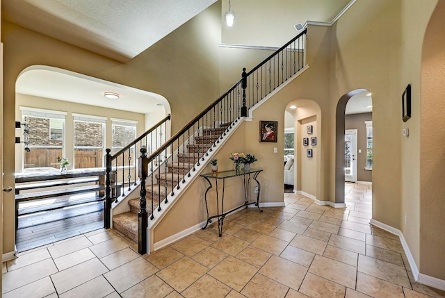 foyer entrance with baseboards, arched walkways, a towering ceiling, stairway, and tile patterned floors