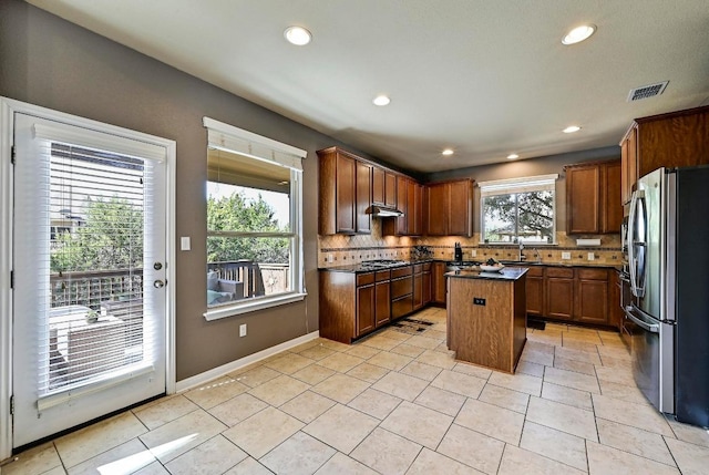 kitchen with a center island, visible vents, decorative backsplash, freestanding refrigerator, and under cabinet range hood