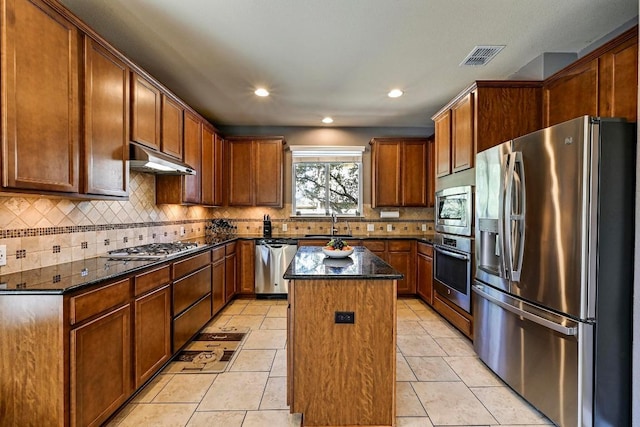 kitchen with under cabinet range hood, stainless steel appliances, a sink, visible vents, and a center island