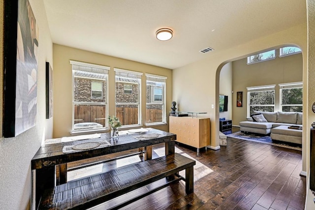 dining room with baseboards, visible vents, arched walkways, and dark wood-type flooring