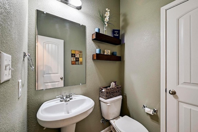 half bath with a textured wall, a sink, and toilet