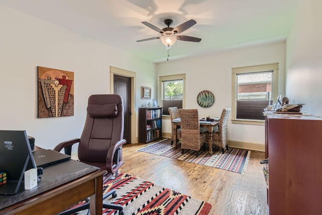 office area with baseboards, wood finished floors, a ceiling fan, and a healthy amount of sunlight