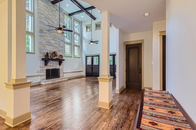 foyer entrance with ceiling fan, dark wood-style flooring, a high ceiling, ornate columns, and a fireplace