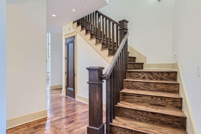 stairway with baseboards, wood finished floors, and recessed lighting