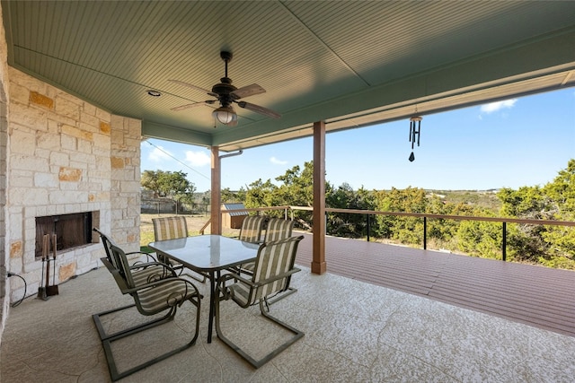 exterior space featuring an outdoor stone fireplace, outdoor dining area, and a ceiling fan