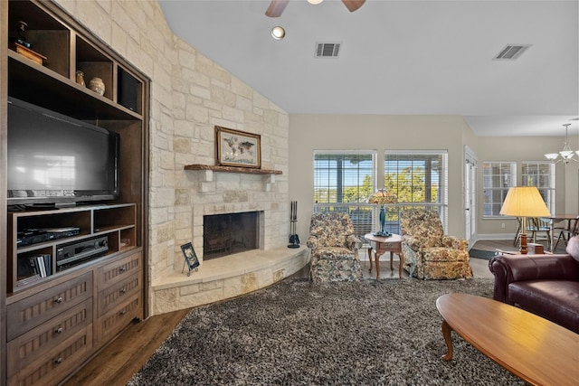 living area with vaulted ceiling, a stone fireplace, dark wood-style flooring, and visible vents