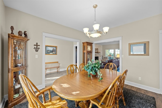 dining space with a large fireplace, baseboards, wood finished floors, and a notable chandelier