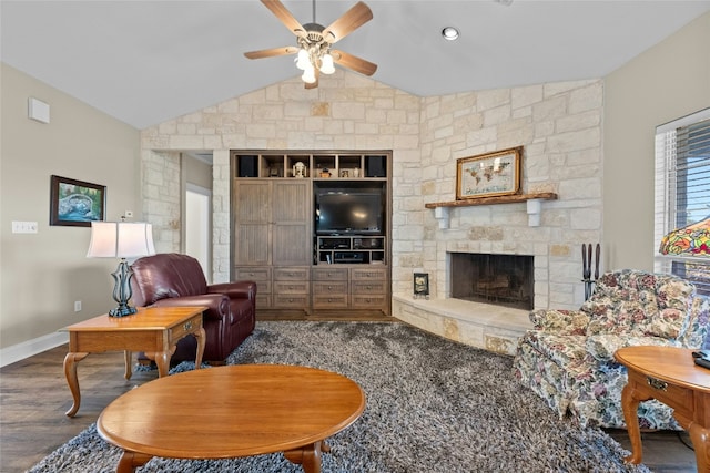 living room with baseboards, lofted ceiling, ceiling fan, wood finished floors, and a stone fireplace