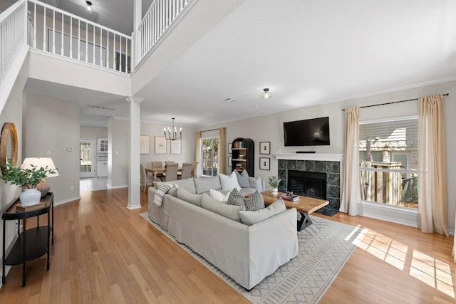 living room featuring a wealth of natural light, ornate columns, light wood-style flooring, and a tile fireplace